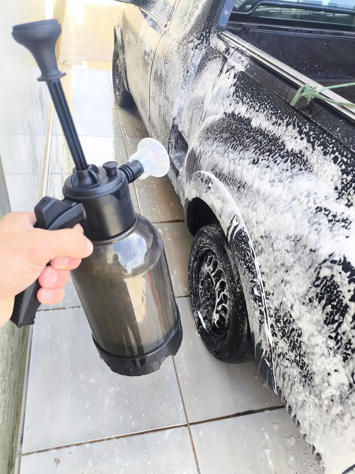 Carro coberto de espuma na calçada durante a lavagem com o pulverizador manual
